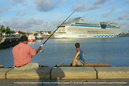 Die Kanaren: Armut durch Massentourismus – Ein älterer Mann und ein Junge angeln am Hafen. Im Hintergrund liegt ein Kreuzfahrtschiff