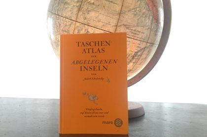 Das Bild zeigt das Buch Taschenatlas der Abgelegenen Inseln und einen Globus. Das Buch lehnt an dem Globus. Der Globus leuchtet von innen.